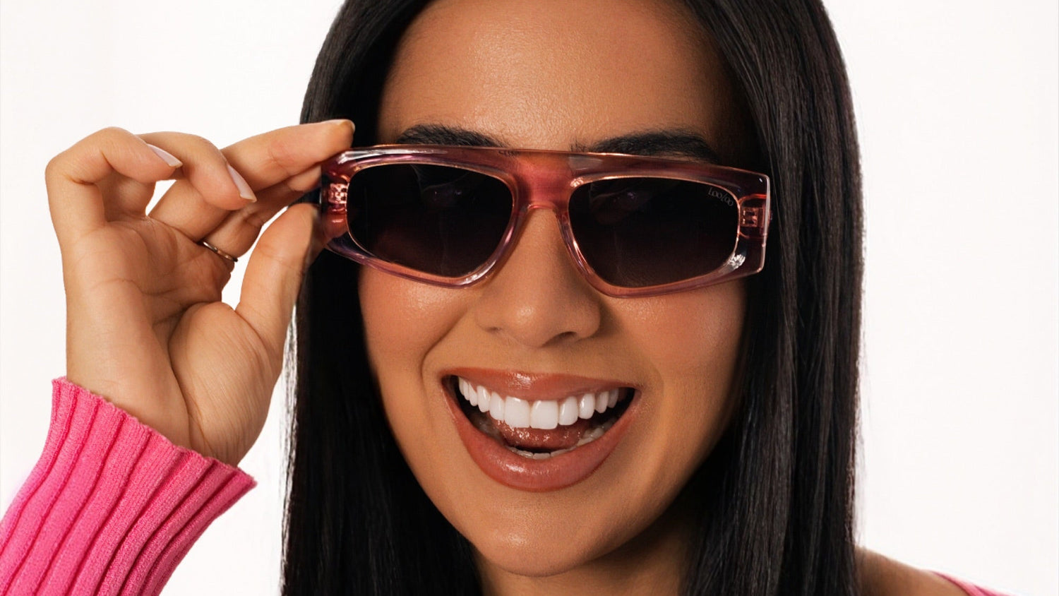 Woman wearing pink shirt, wearing a pair of pink acetate frame sunglasses, on a white background.