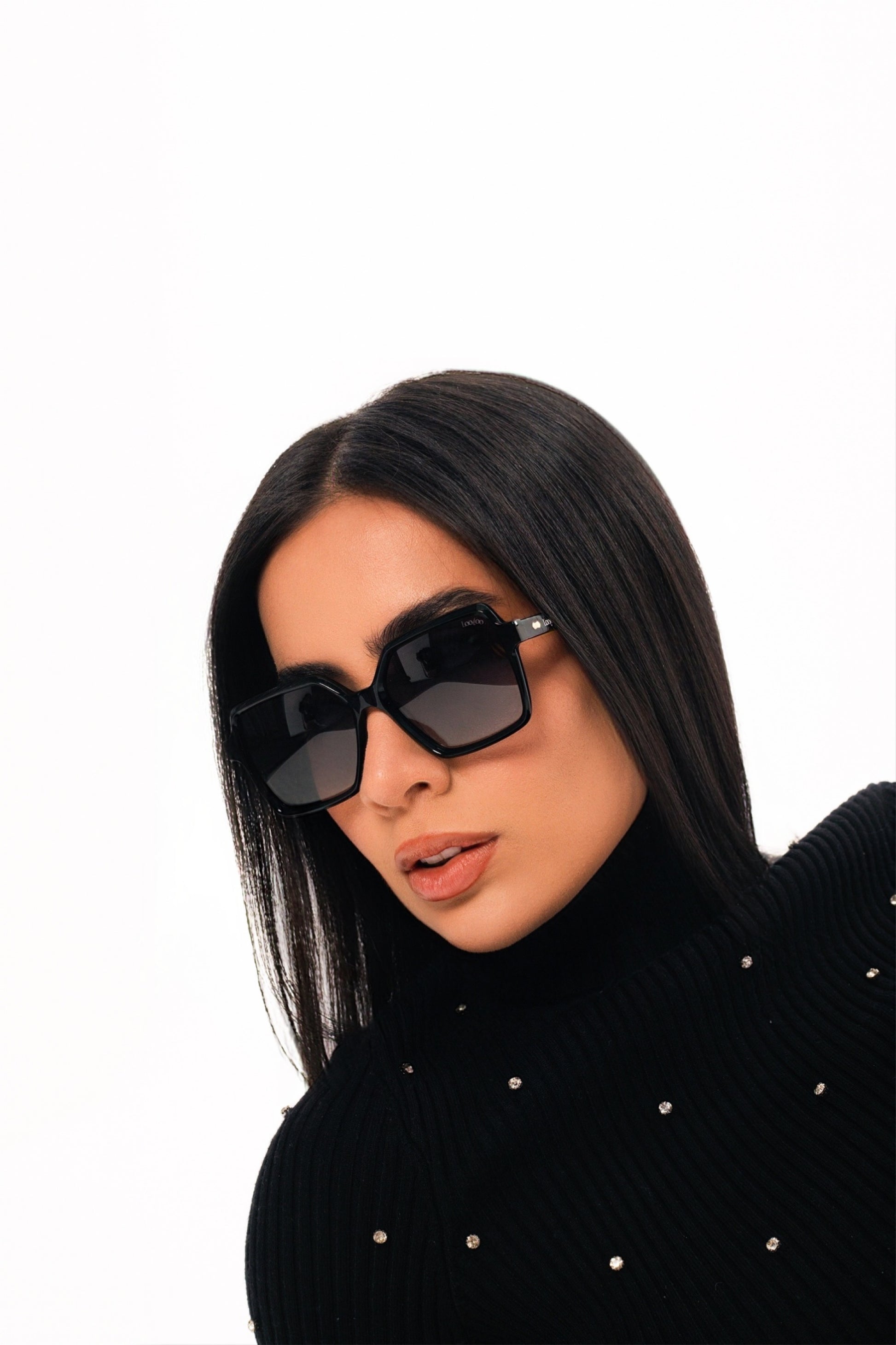 Woman wearing black sweater, wearing a pair of black acetate frame sunglasses with gradient lenses, on a white background.