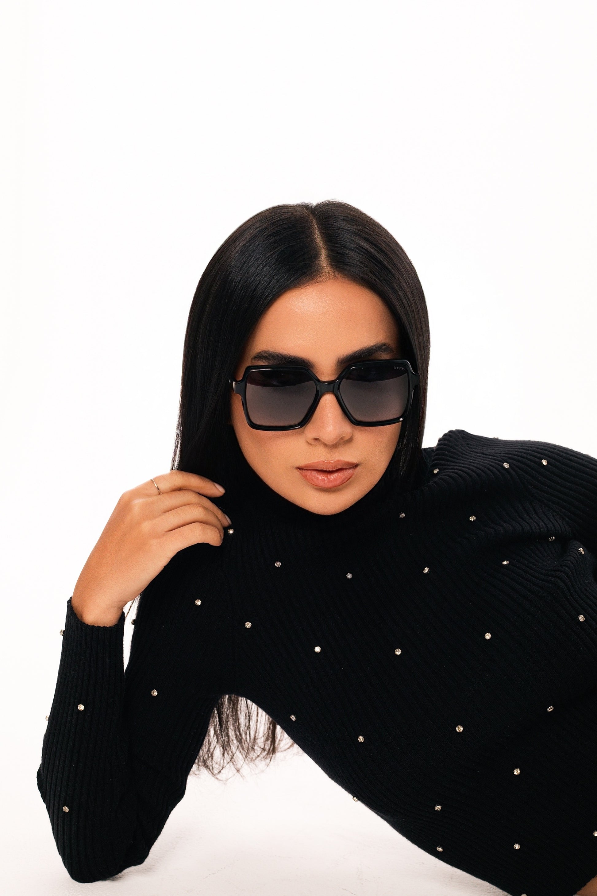 Woman wearing black sweater, wearing a pair of black acetate frame sunglasses with gradient lenses, on a white background.