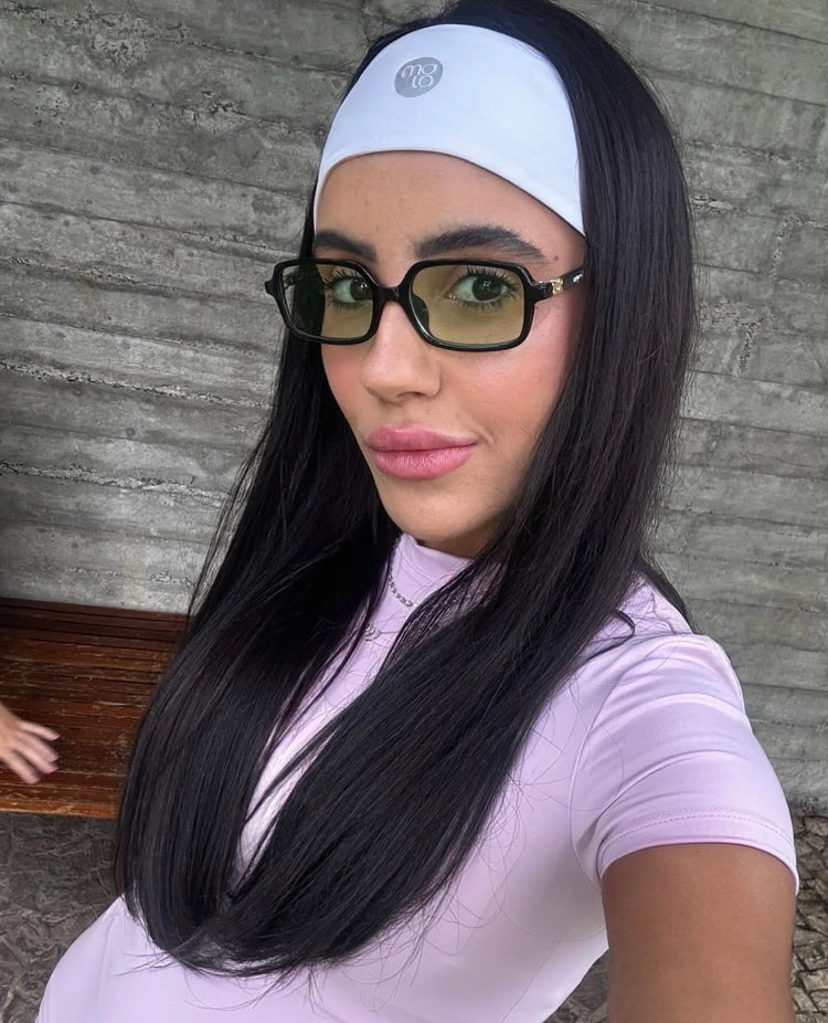 Woman wearing a white headband, light pink shirt and glasses with a neutral background