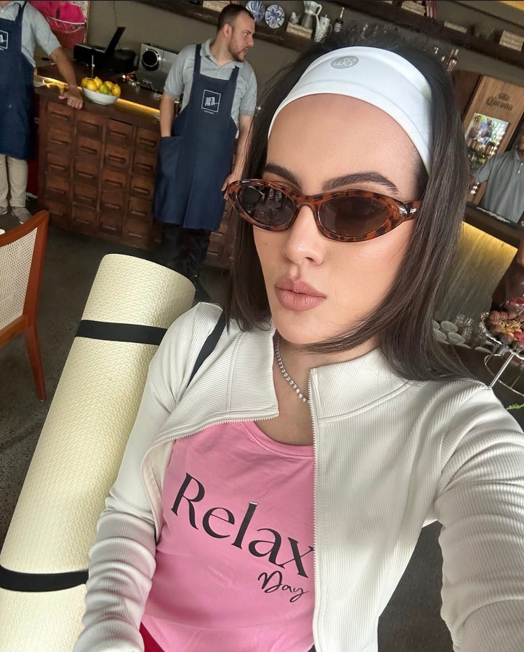 Woman wearing tortoise frame sunglasses and a white headband, and rolled yoga mat on shoulder in a restaurant setting