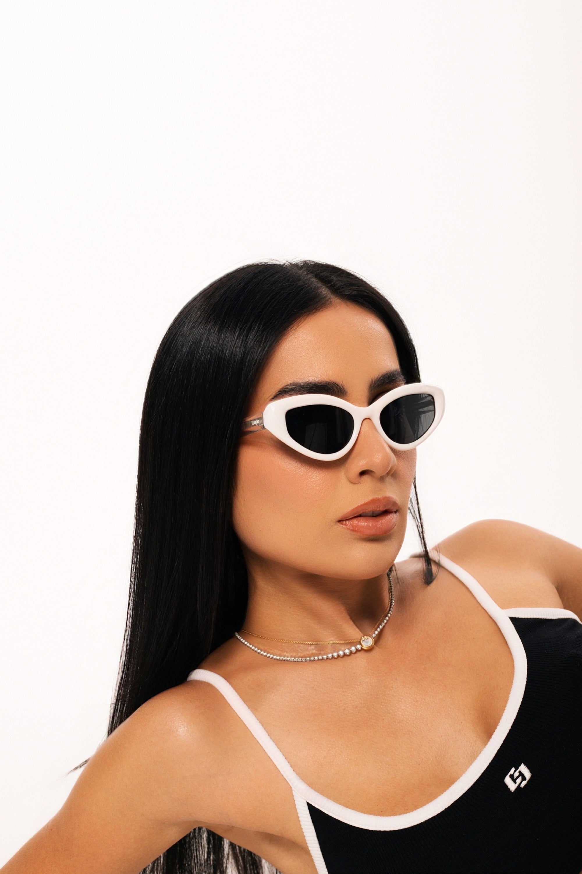 Woman wearing a black top, wearing a pair of white and crystal acetate frame sunglasses, on a white background.