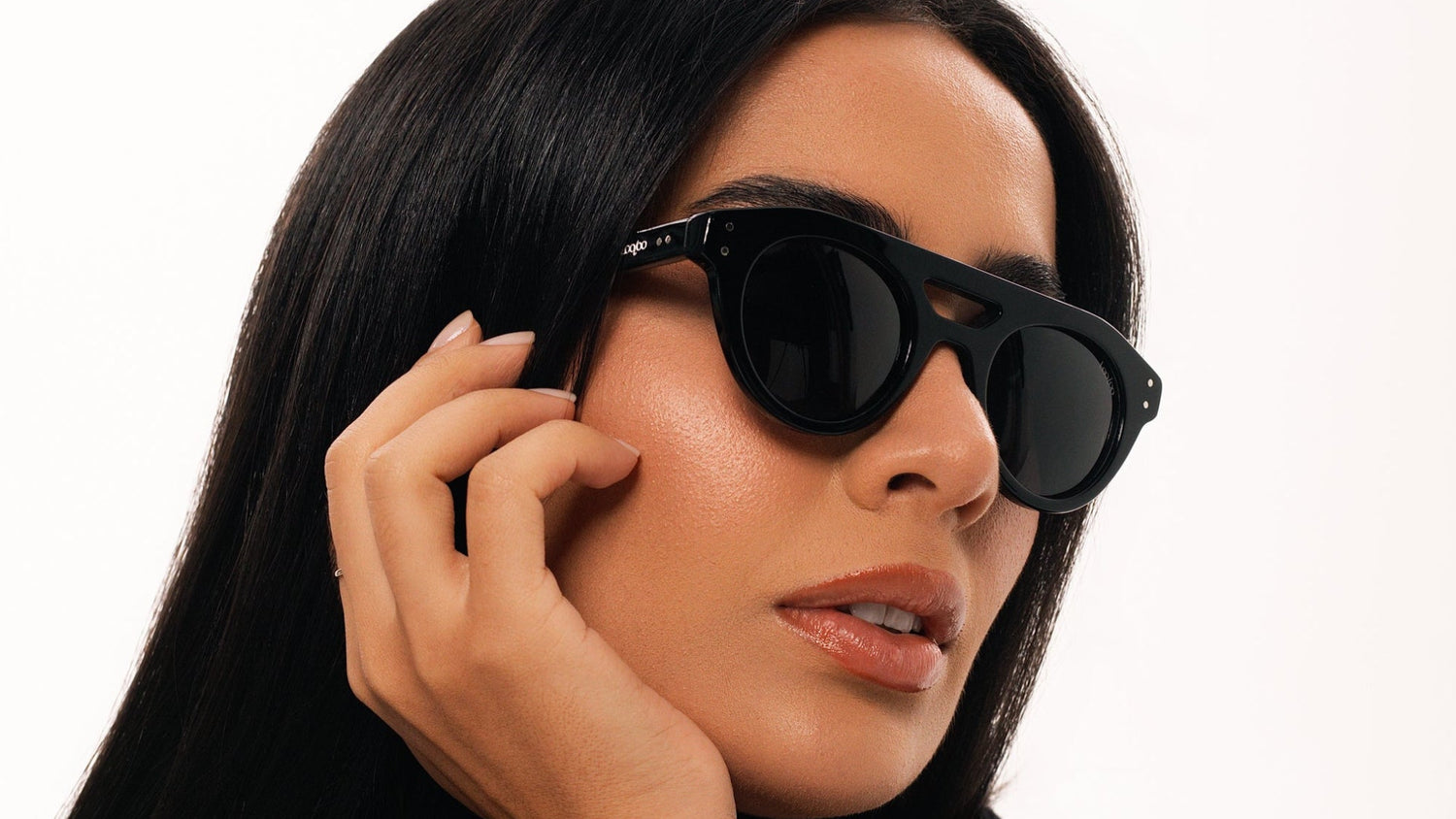 Woman wearing black sweater, wearing a pair of black acetate frame  sunglasses, on a white background.