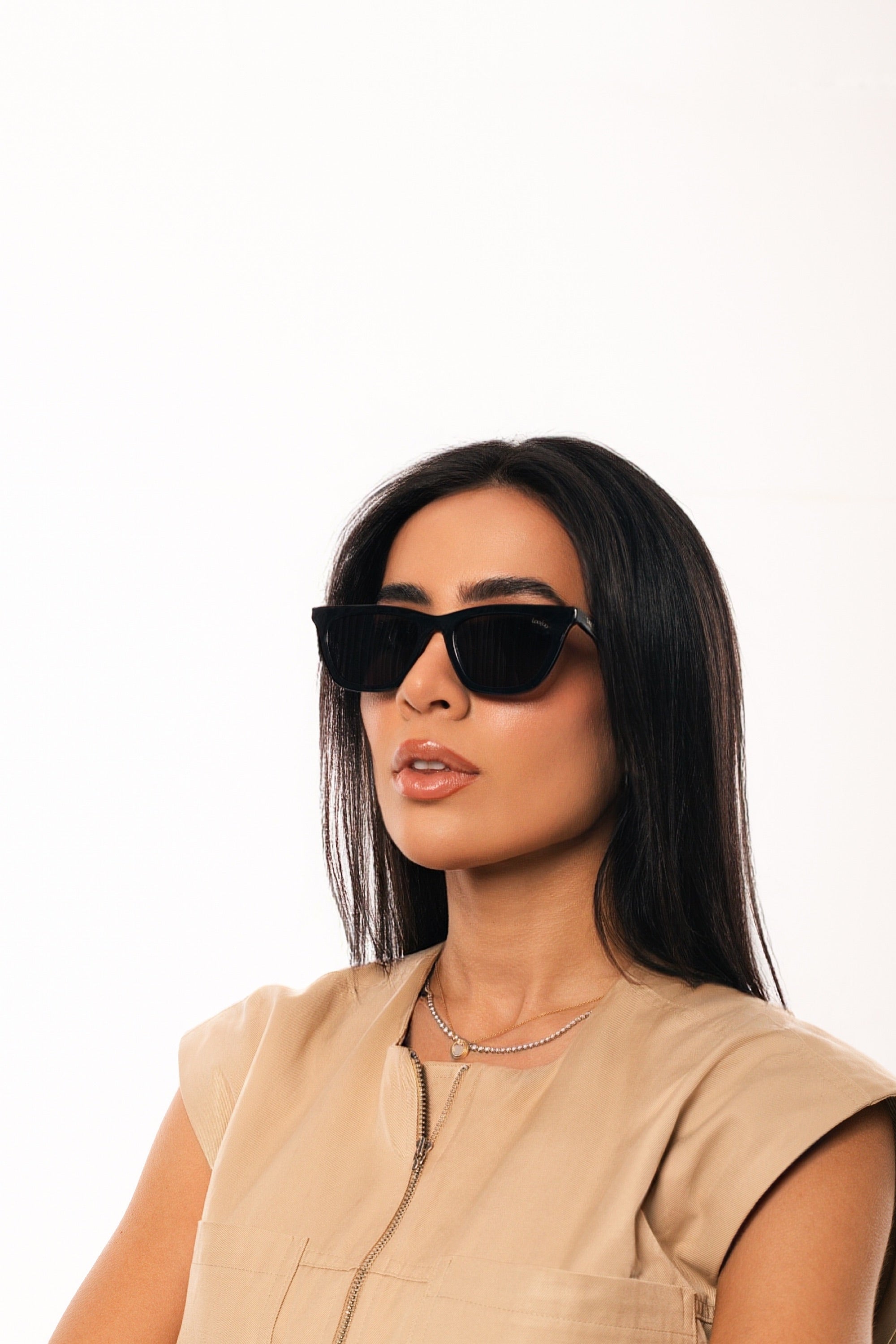 Woman wearing beige shirt, wearing a pair of black acetate frame sunglasses, on a white background.