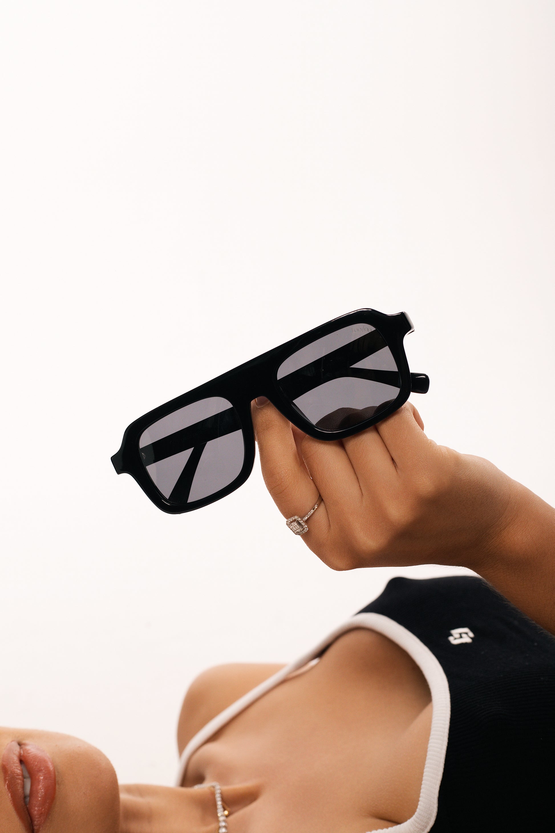 Woman with black outfit holding a pair of black acetate frame on a white background.