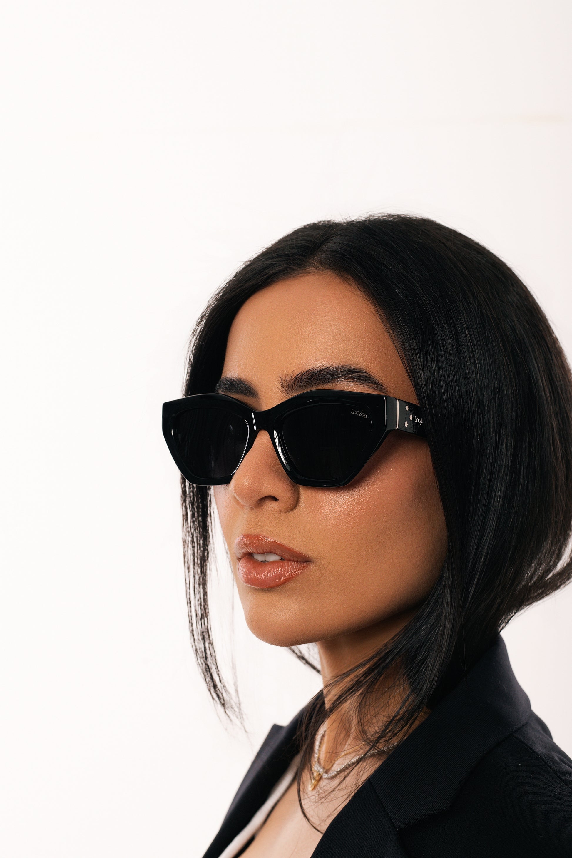 Woman wearing black jacket, wearing a pair of black acetate frame sunglasses, on a white background.
