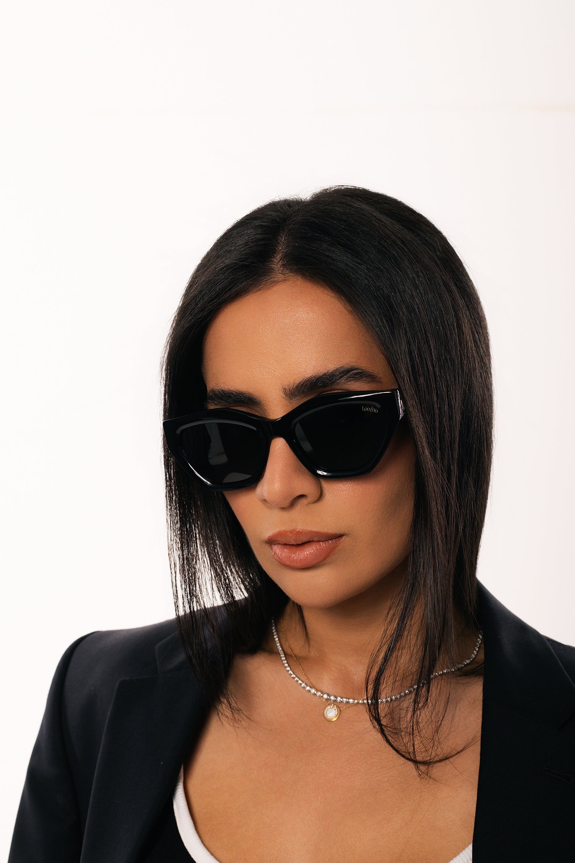 Woman wearing black jacket, wearing a pair of black acetate frame sunglasses, on a white background.