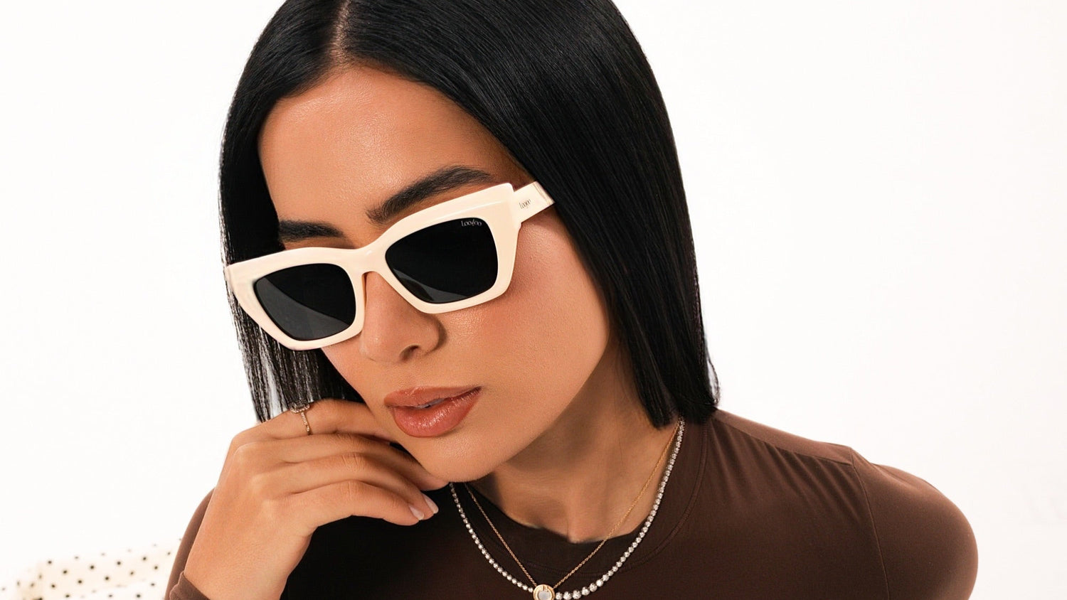 Woman wearing brown outfit, wearing a pair of beige acetate frame sunglasses, on a white background.