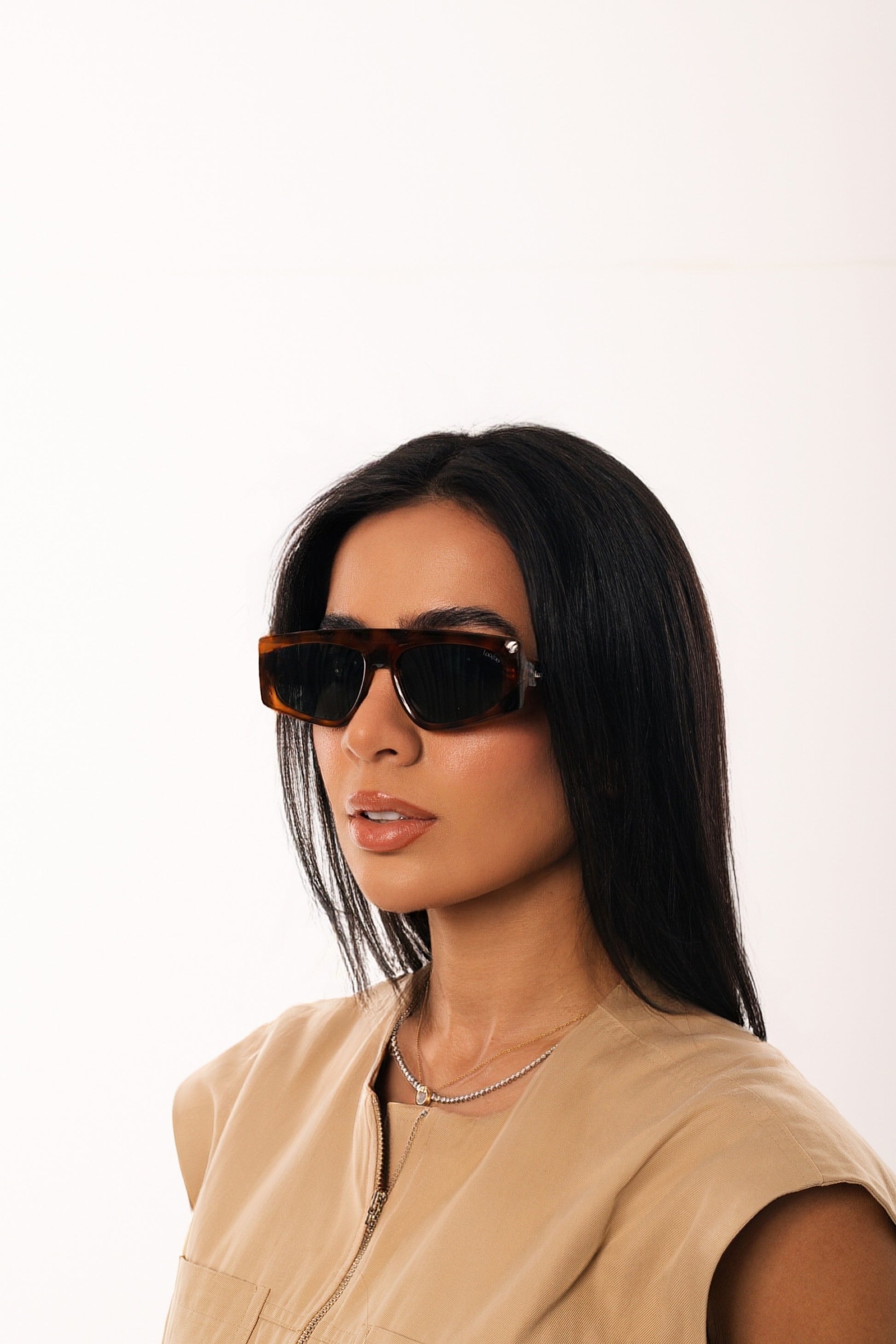 Woman wearing beige shirt, wearing a pair of tortoise acetate frame sunglasses, on a white background.