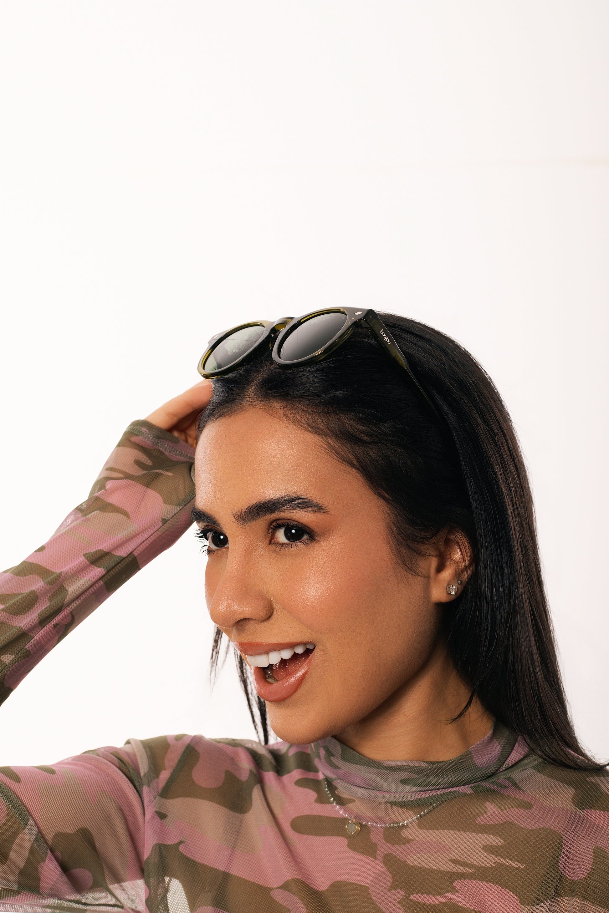 Woman wearing camouflage shirt, holding a pair of green acetate frame and green lenses sunglasses, on a white background.