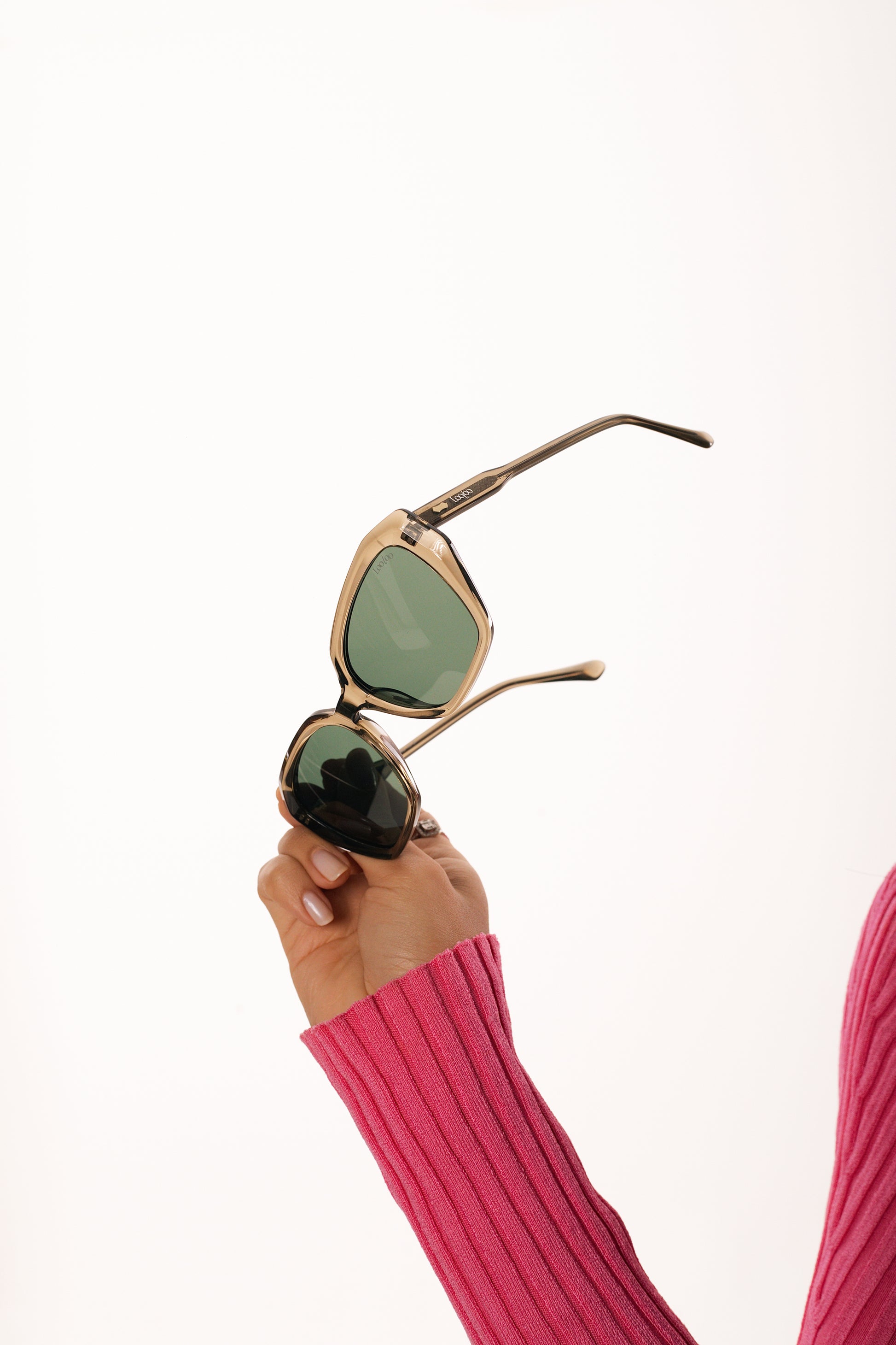 Woman wearing pink sleeve holding a pair of green acetate frame and green lenses sunglasses, on a white background
