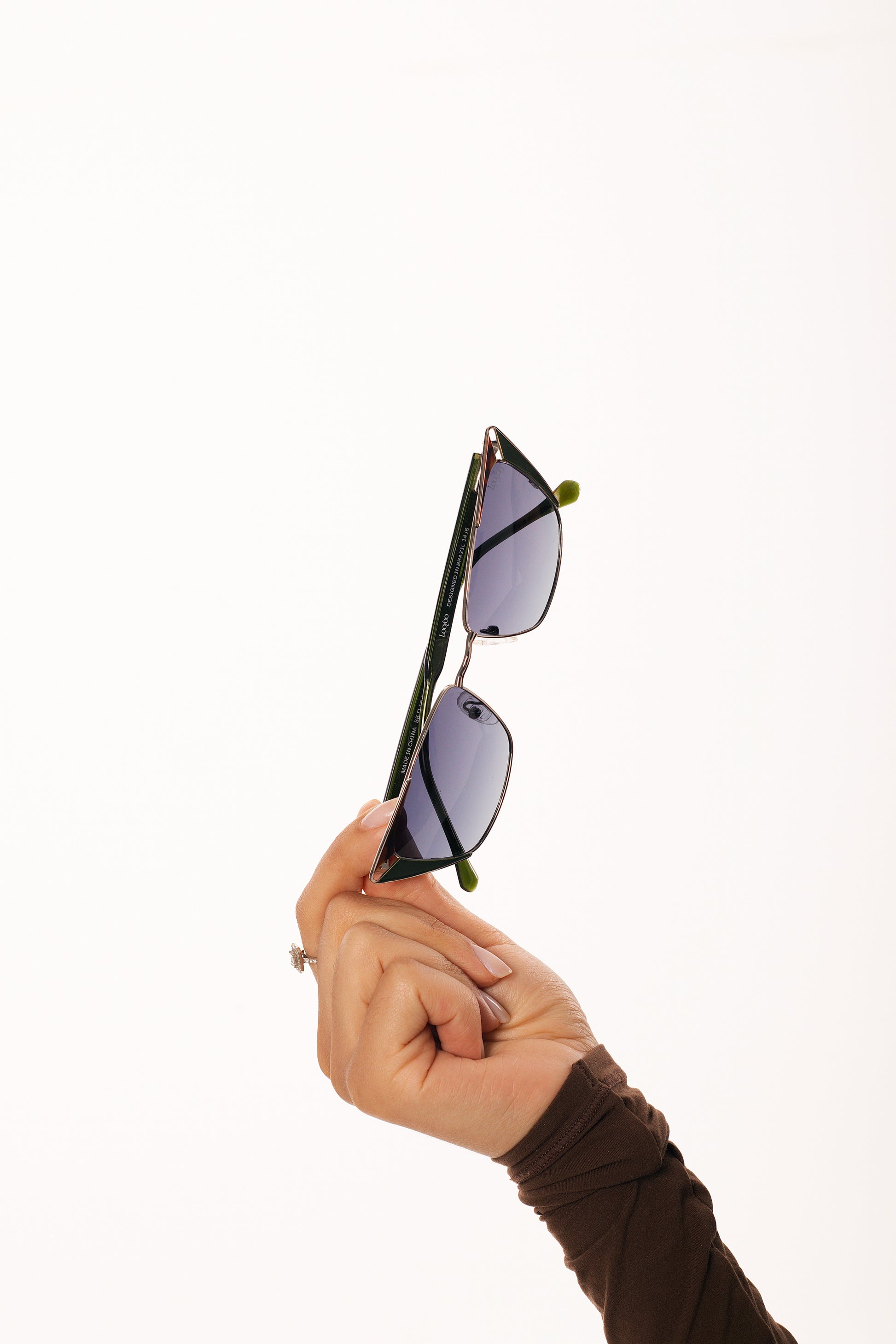 Woman wearing brown outfit, holding a pair of black acetate and metal frame sunglasses, on a white background.